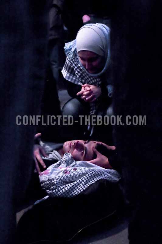 Photograph of a young muslin nurse watching over an injured protester in bus shelter.
